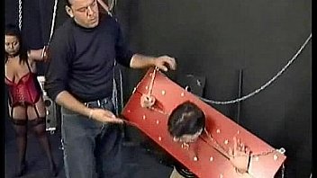 Two scared slaves tied with their arms and head in a dungeon are hit and spanked by master